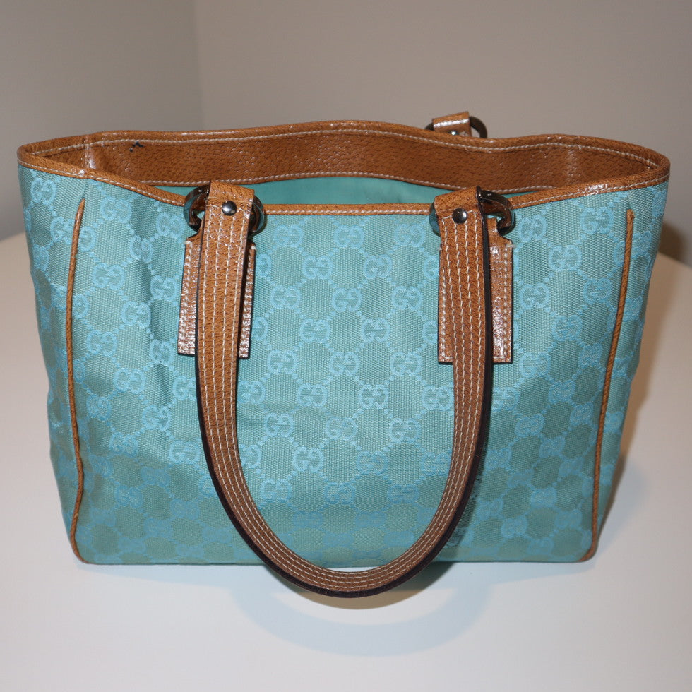 teal/turquoise Gucci canvas monogram handbag with brown handles on a white surface