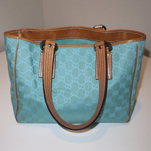 teal/turquoise Gucci canvas monogram handbag with brown handles on a white surface